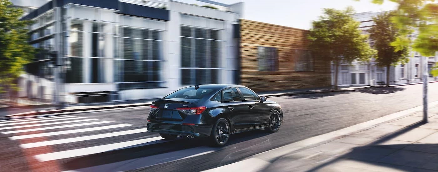 A black 2023 Honda Civic Sport is shown from a rear angle driving on a city street.