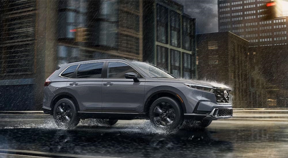 A grey 2024 Honda CR-V Sport Touring driving through a city in the rain.