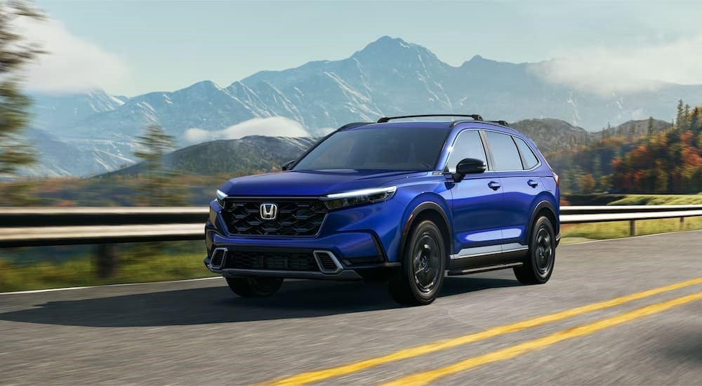 A blue 2024 Honda CR-V Sport Touring Hybrid driving on a mountain road to a Honda dealer near Picnic Point-North Lynnwood.