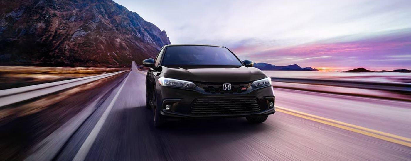 A black 2023 Honda Civic Si is shown on a coastal road after visiting a Honda dealer near Bellevue.