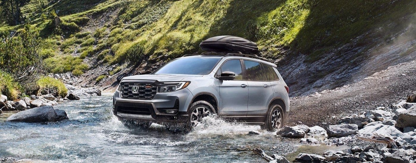 A silver 2023 Honda Passport TrailSport is shown driving through a creek.