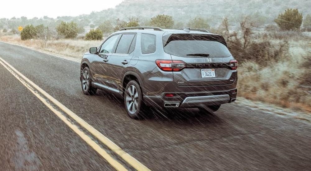 A gray 2023 Honda Pilot is shown driving on a rainy day.