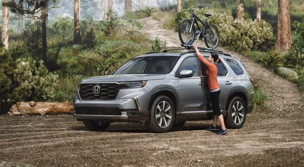 A silver 2023 Honda Pilot for sale is shown parked near the forest.