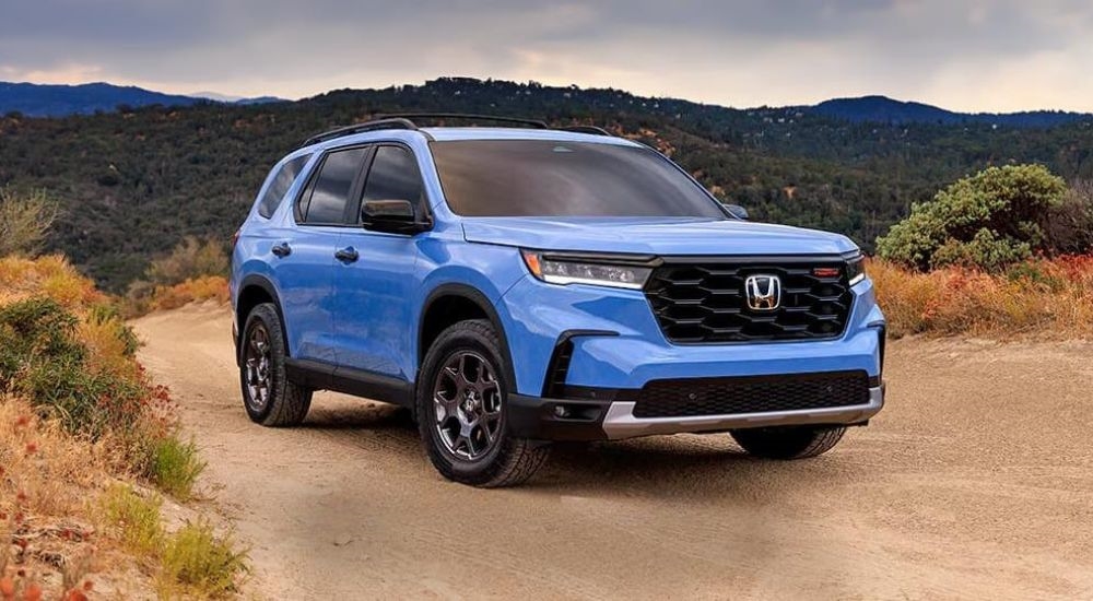 A blue 2025 Honda Pilot Trailsport is shown on a trail after visiting a Honda dealer near Bellevue.