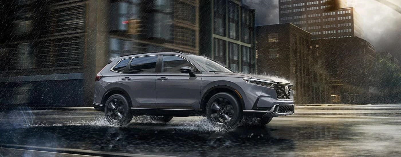 A grey 2023 Honda CR-V Sport Touring Hybrid is shown driving on a city street in the rain.