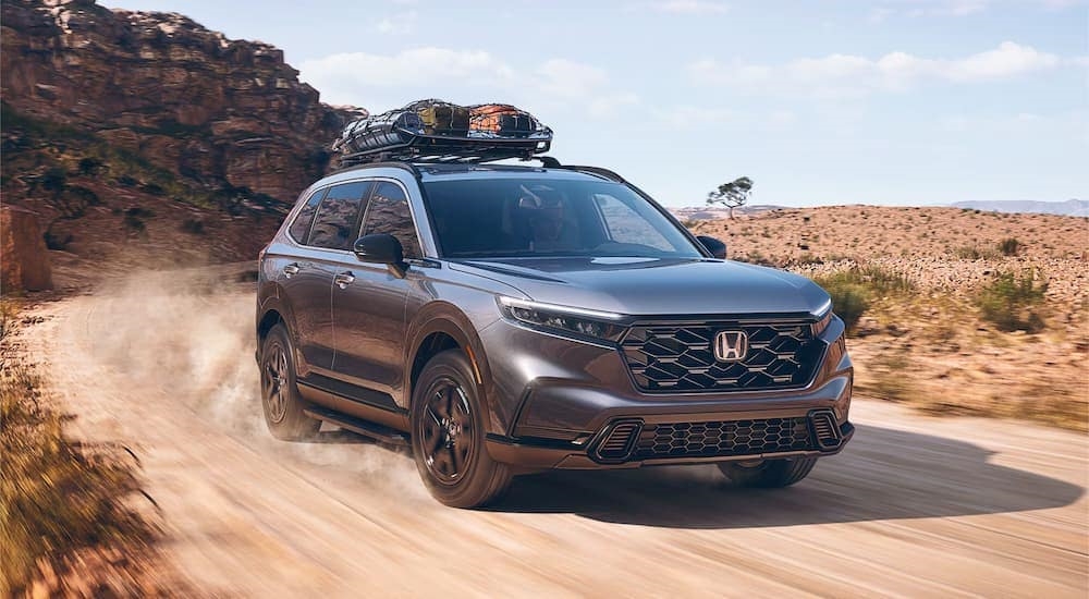 A 2024 Honda CR-V Sport Touring Hybrid with gear in the rooftop cargo net driving on a dirt trail.