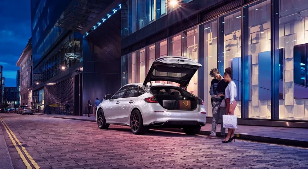 A white 2024 Honda Civic for sale is shown in front of a shop.