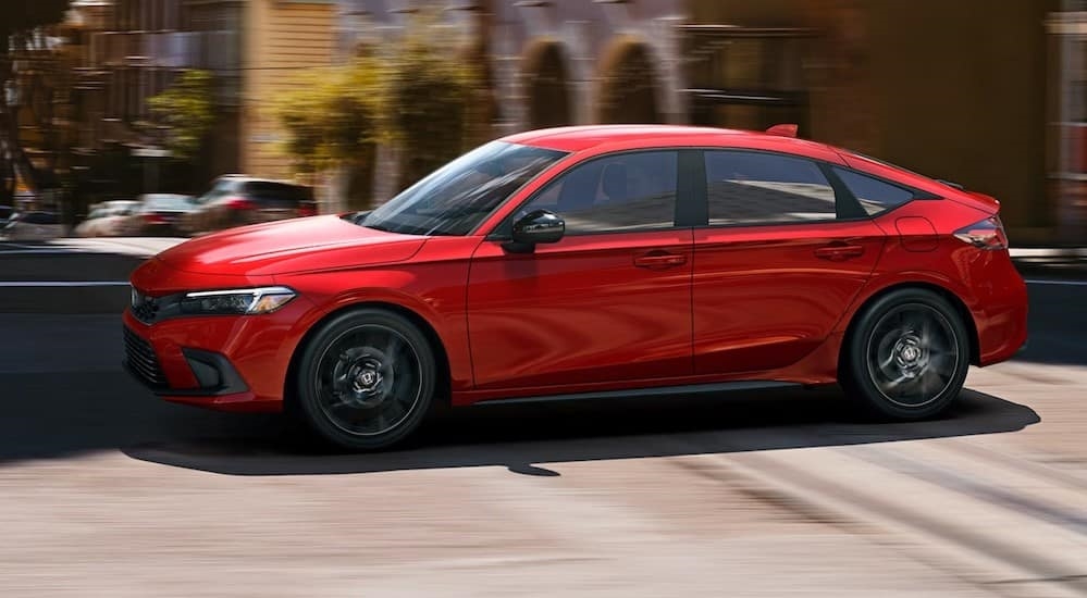 A red 2024 Honda Civic Hatchback is shown driving on a city street.