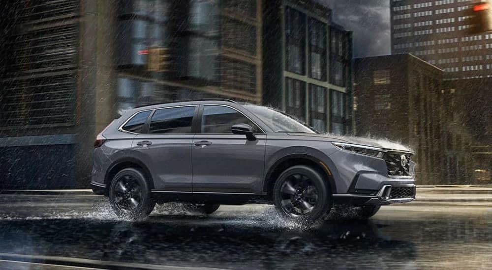 A grey 2023 Honda CR-V Sport Touring Hybrid is shown driving through a rainy city.