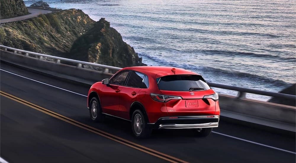 A red 2023 Honda HR-V is shown from the rear at an angle on a coastal road.