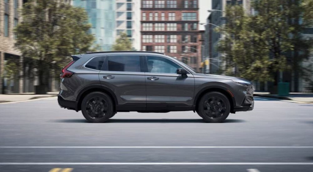 A grey 2023 Honda CR-V is shown from the side driving on a city street.