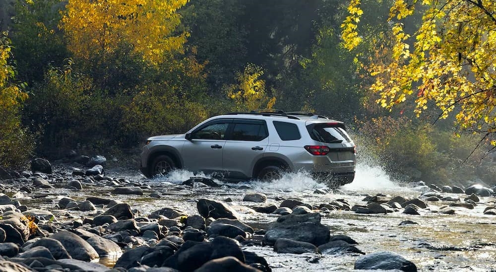 A silver 2023 Honda Pilot Trailsport is shown driving though a river after leaving a Honda dealer.