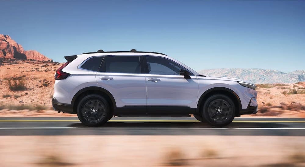 A white 2023 Honda CR-V Sport Touring Hybrid for sale near Lynnwood, WA is shown from the side while driving through a desert.