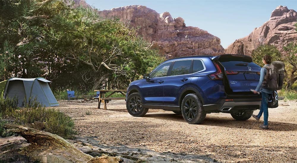 A blue 2023 Honda CR-V Sport Touring Hybrid is shown from the rear while parked at a campsite.