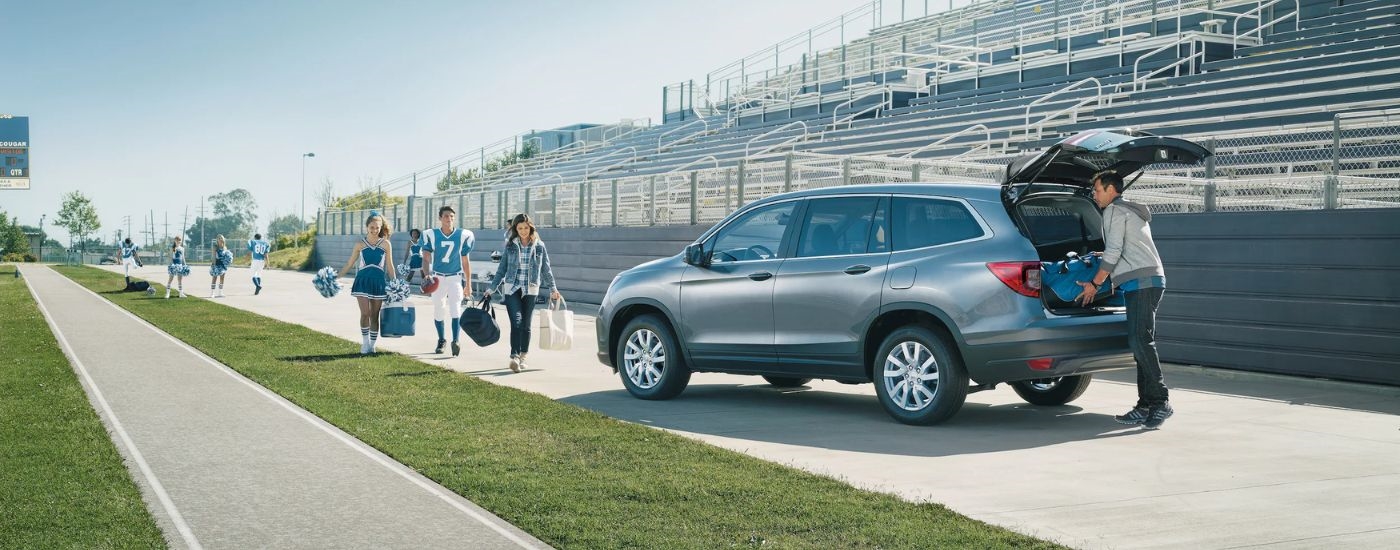 A grey 2021 Honda Pilot is shown from the rear at an angle while being loaded with sports equipment.