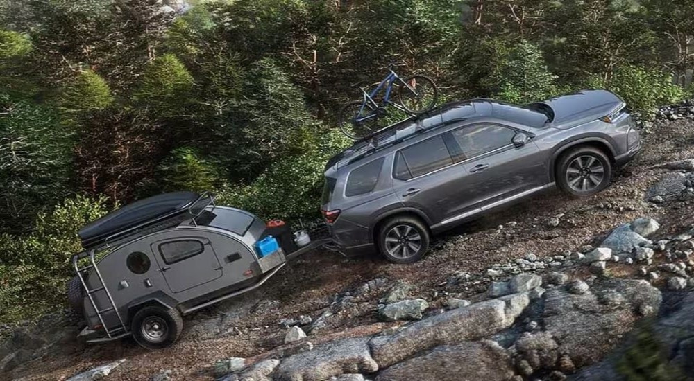 A silver 2024 Honda Pilot Touring towing a teardrop trailer up a mountain.