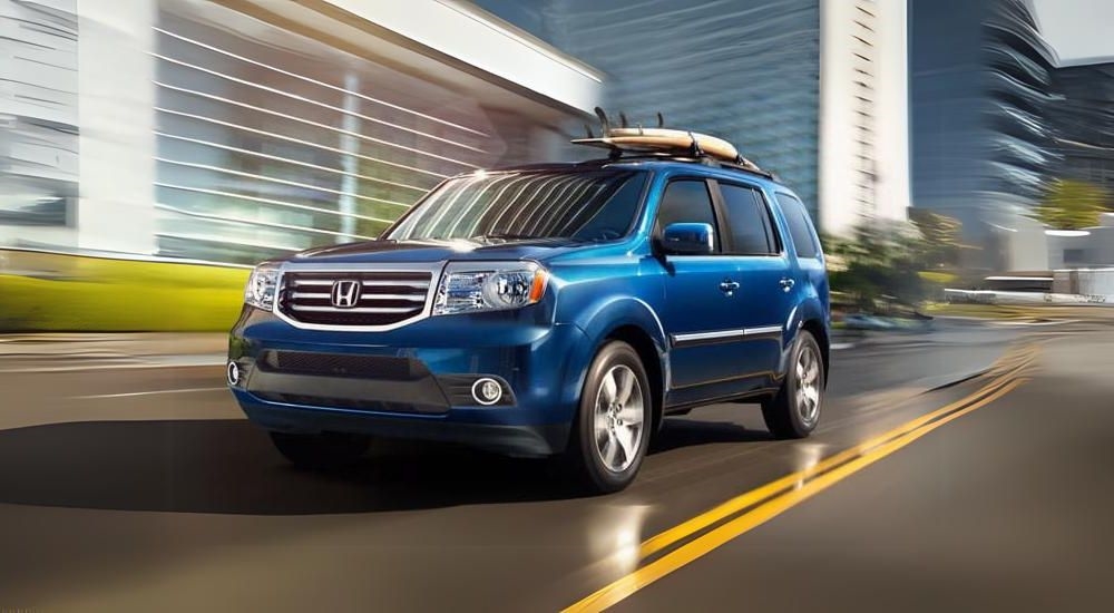 A blue 2015 used Honda Pilot for sale is shown driving on a city street.