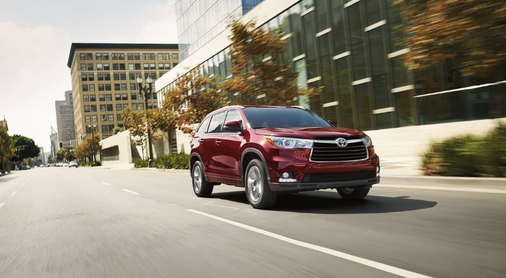 A maroon 2016 Toyota Highlander is shown from the front driving on a city street.