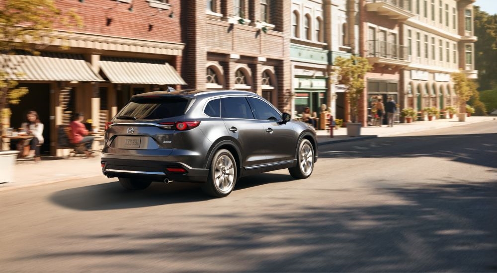 A grey 2018 Mazda CX-9 is shown from the rear driving on a city street.