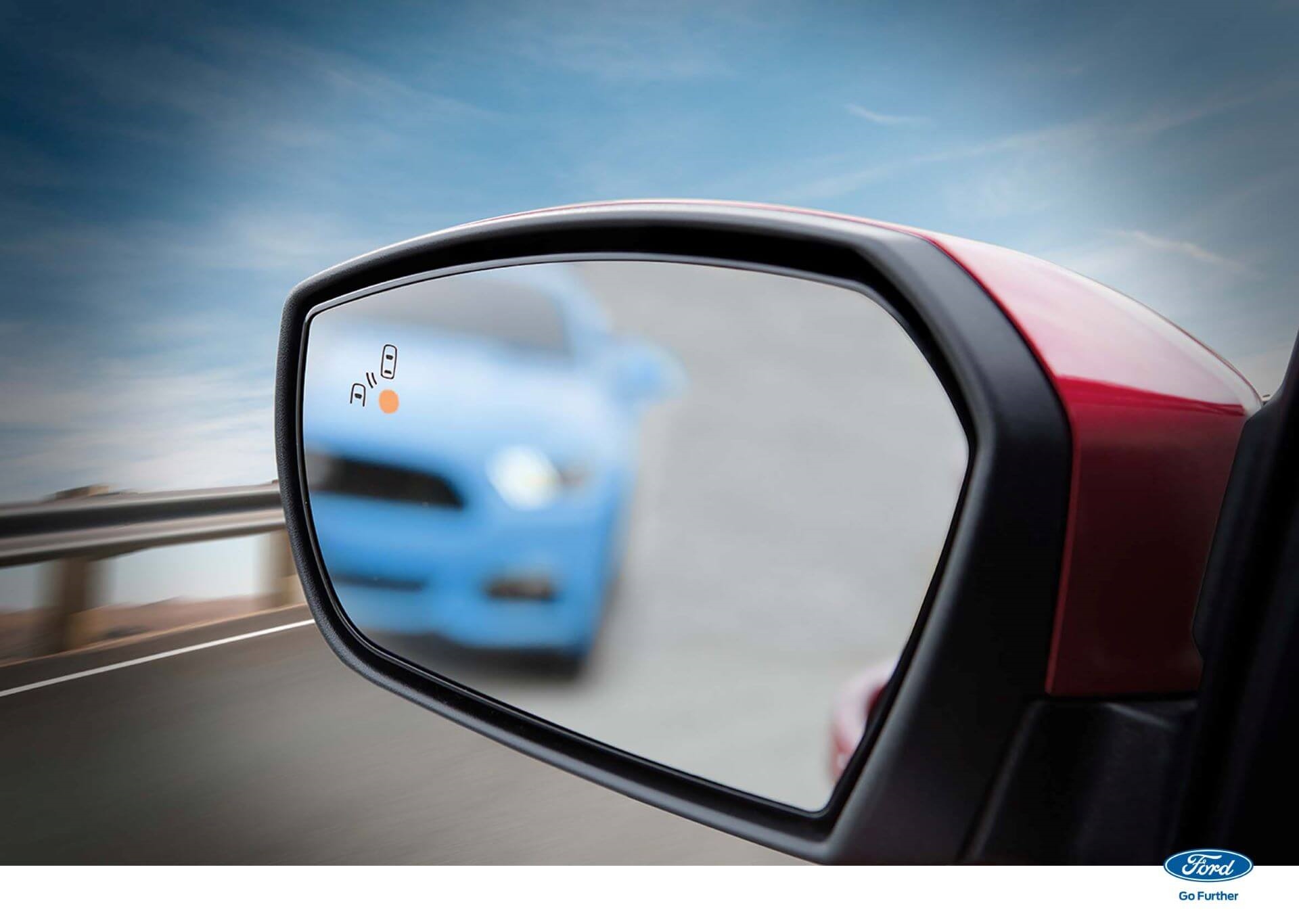 Ford truck alerting driver with BLIS in side mirror shot, showing blue car out of focus in mirror.