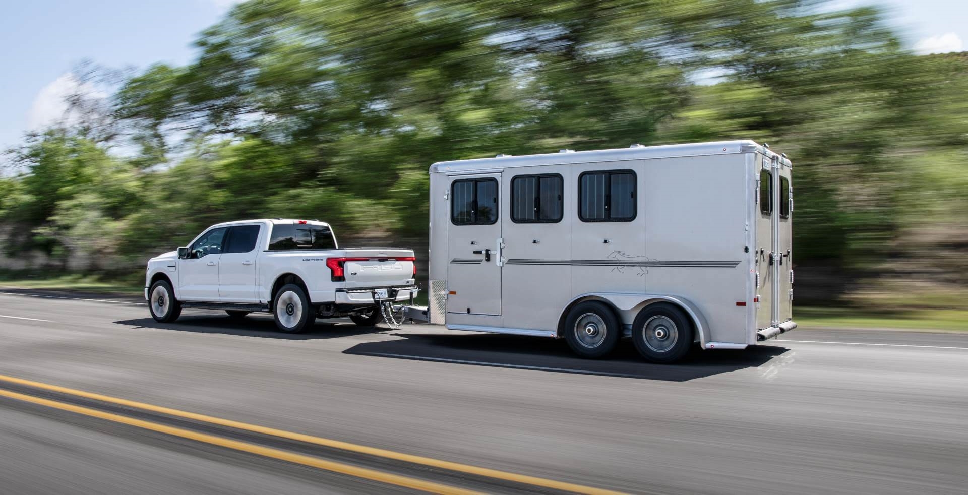 Ford F-150 Lightning towing camping trailer along treed So Cal 2-lane highway.