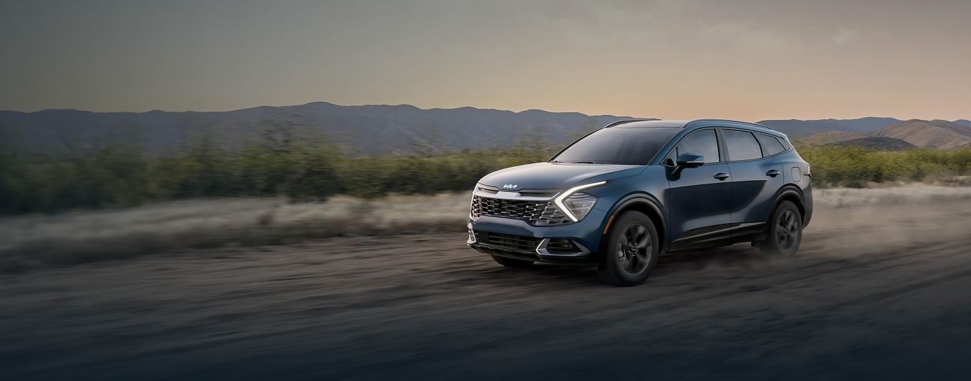 A blue 2024 Kia Sportage driving down a dusty road.