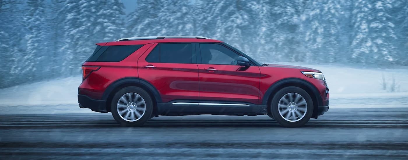 A side angle view of a red 2024 Ford Explorer Limited driving down a snowy road.