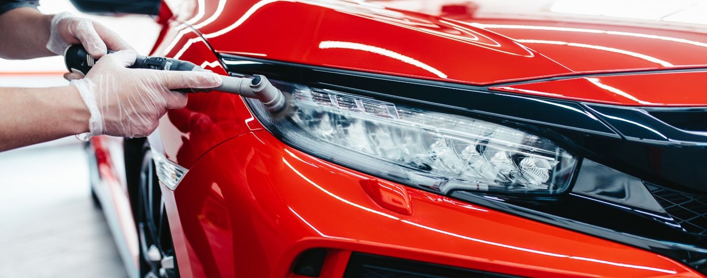 A person is shown doing headlight restoration on a red Honda Civic.