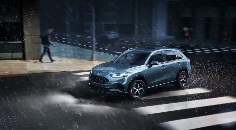 A blue 2025 Honda HR-V EX-L is driving on a city street during a rainstorm.