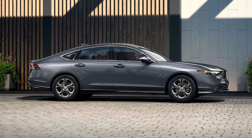 A grey 2024 Honda Accord EX for sale is parked in a driveway next to a wood fence.