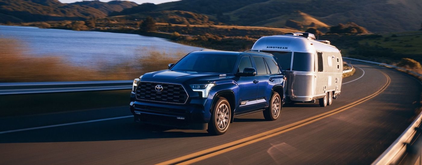 A blue 2024 Toyota Sequoia is shown from the front at an angle while towing a camper.