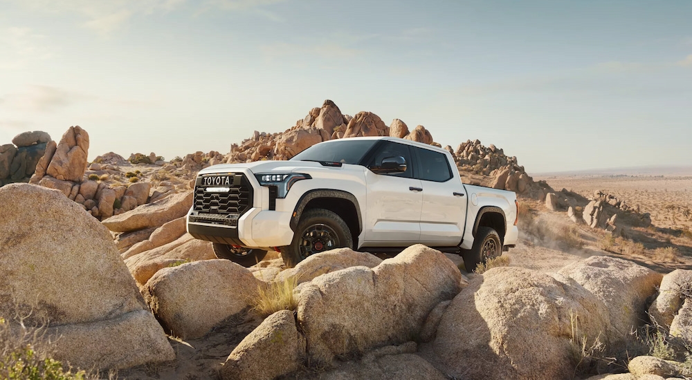 A white 2024 Toyota Trundra TRD Pro off-roading over large boulders.