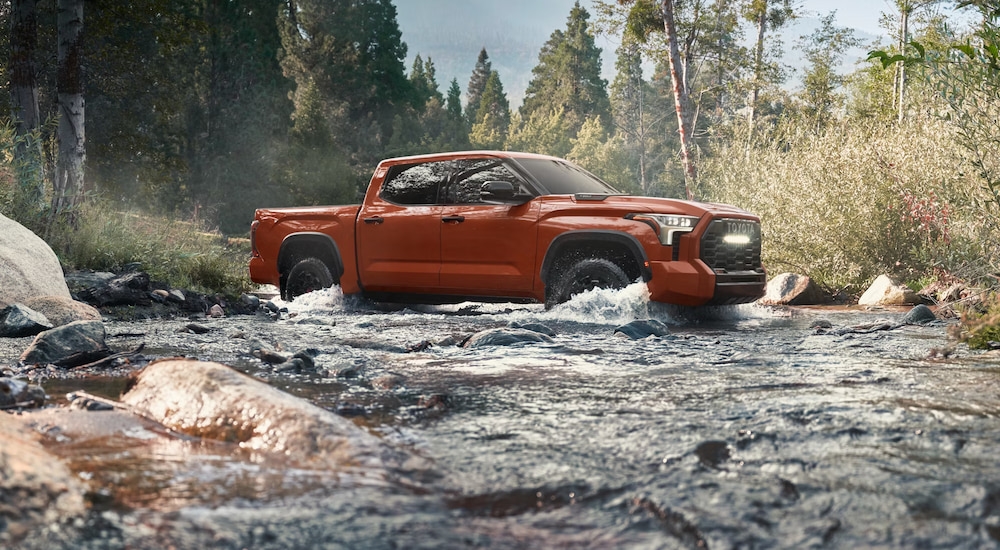 An orange 2024 Toyota Tundra TRD Pro fording a small stream while off-roading.