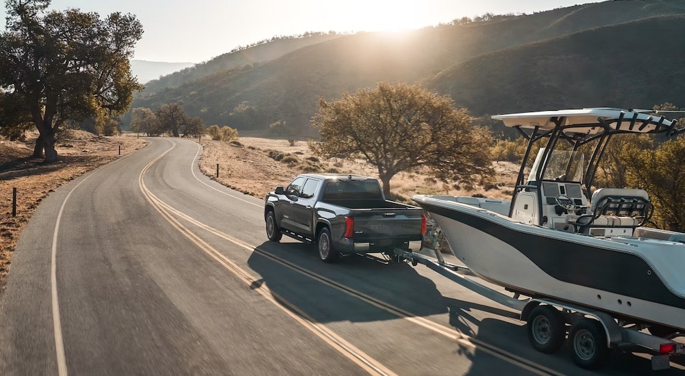 A grey 2024 Toyota Tundra is shown from the rear at an angle while towing a boat.