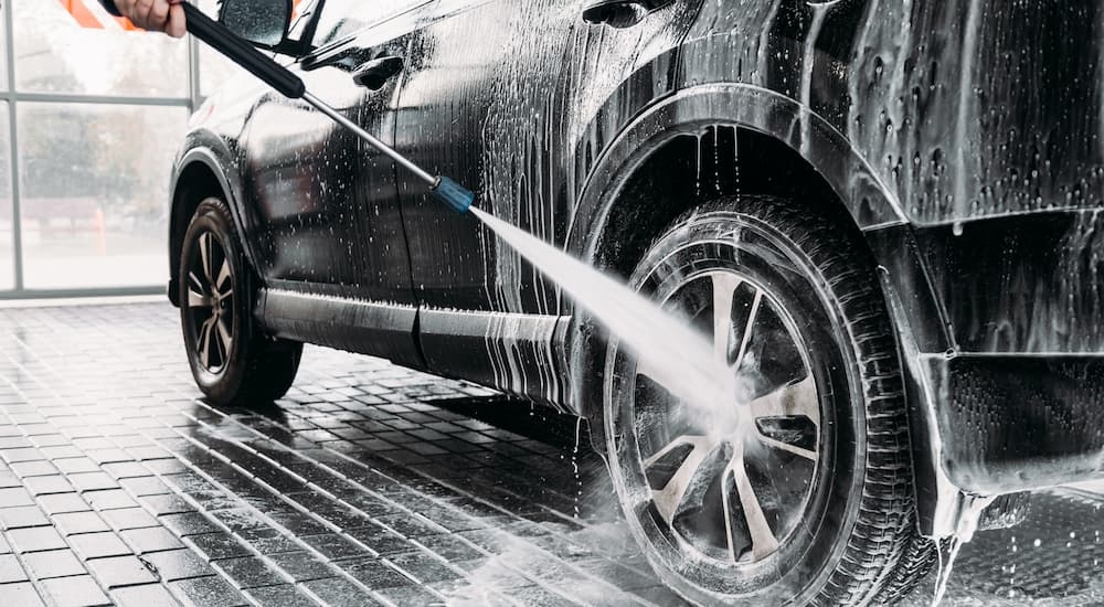 The rim on a black SUV is being powerwashed at a dealership during a car detailing.