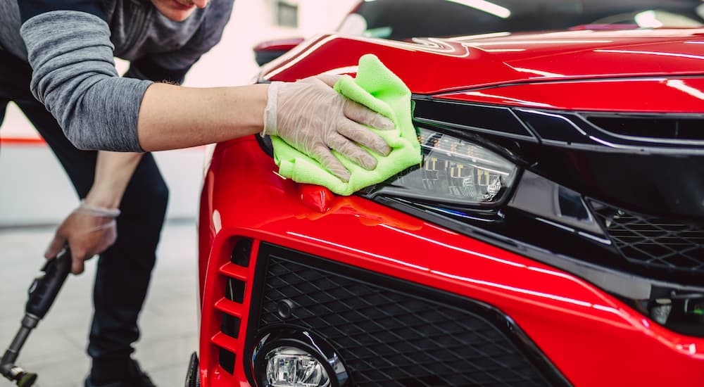 A close up of a person cleaning the headlight on a red vehicle.