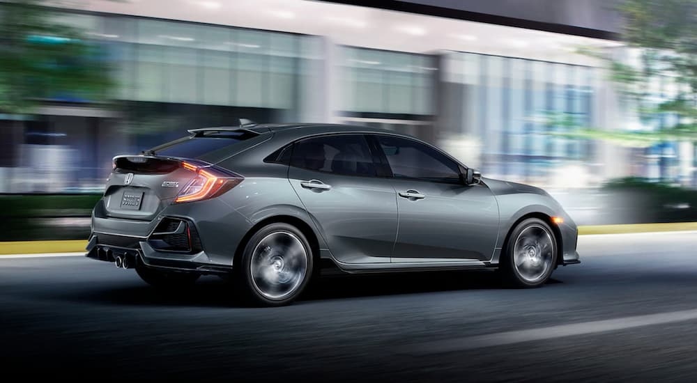 A grey 2020 Honda Civic Hatchback Sport Touring is speeding by a building.