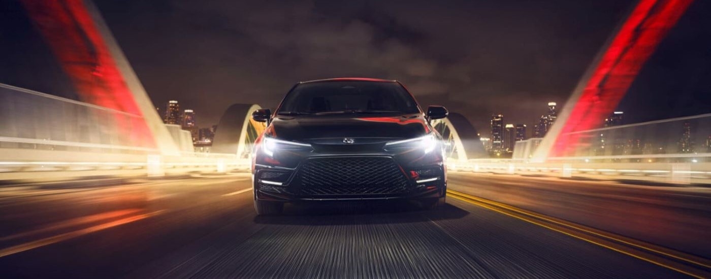 A black 2024 Toyota Corolla Nightshade is shown driving over a bridge after visiting a Toyota dealer.