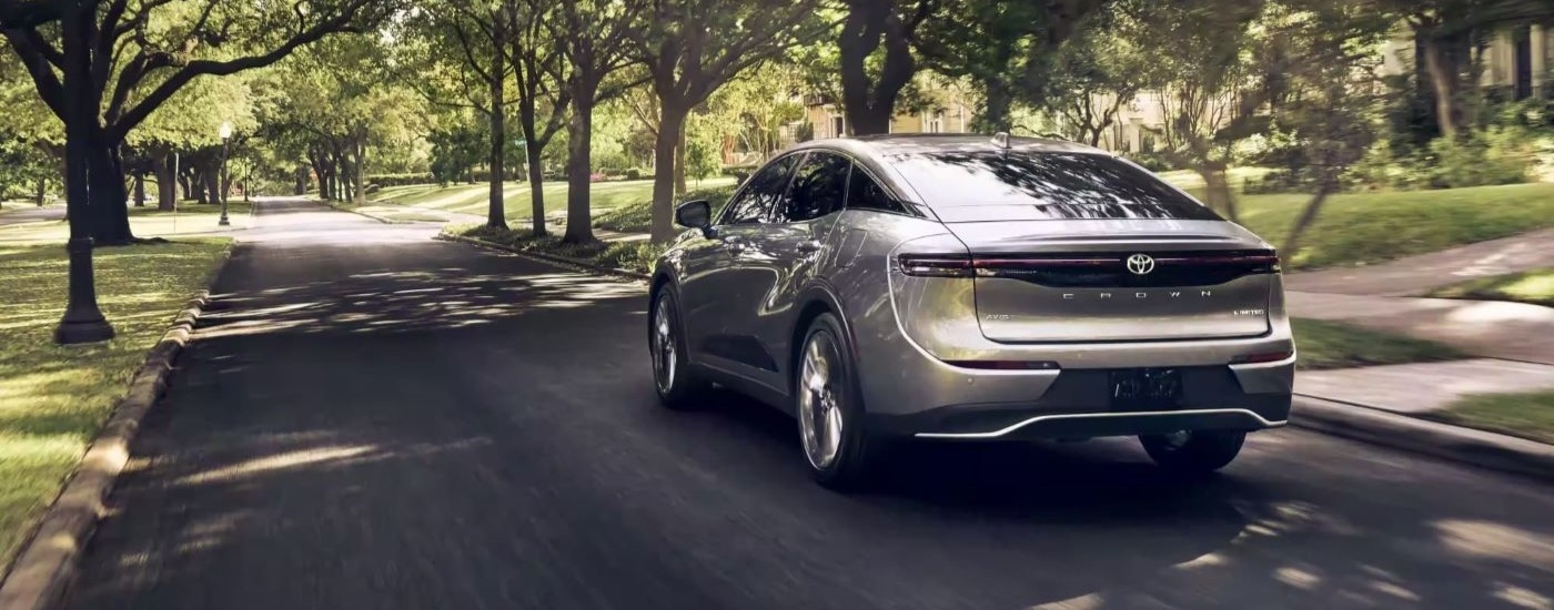 A silver 2023 Toyota Crown Limited is shown from the rear driving on a tree-lined road.