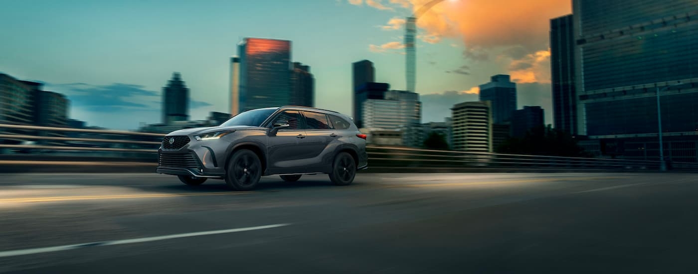 A silver 2021 Toyota Highlander XSE is shown driving past a city.