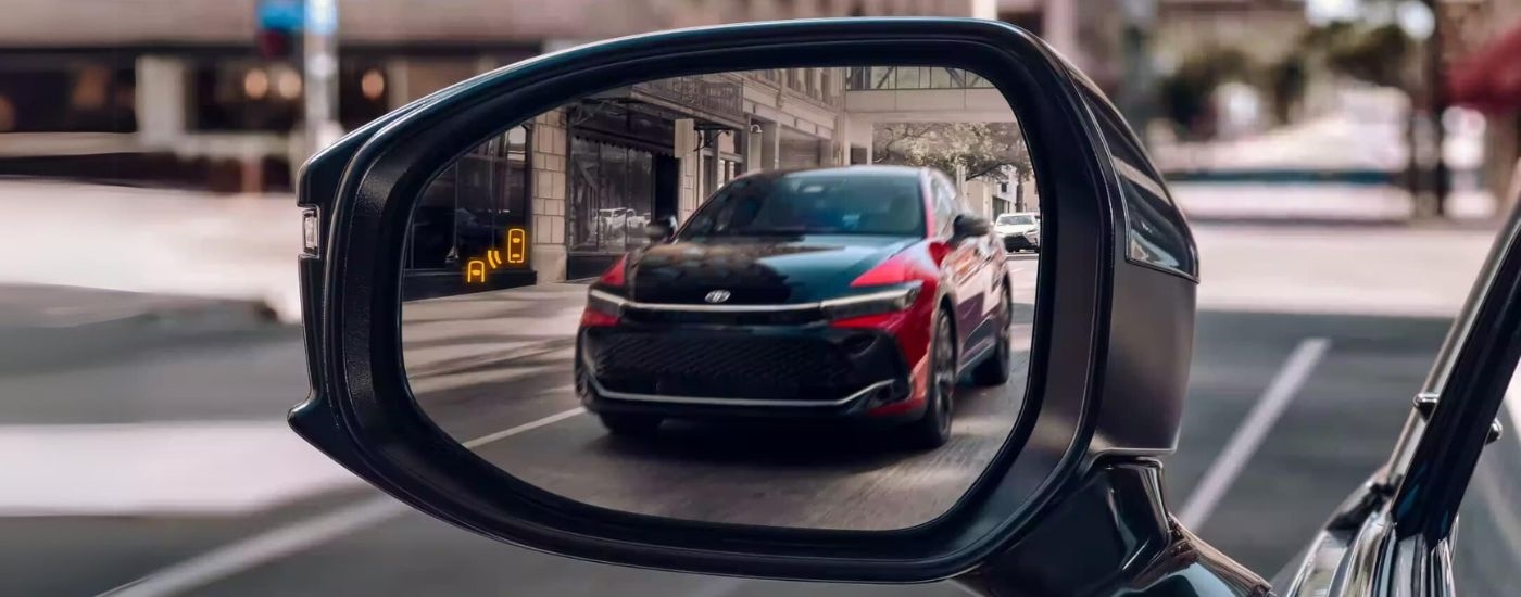 A red and black 2023 Toyota Crown is shown in the rear view mirror of a vehicle driving on a street.