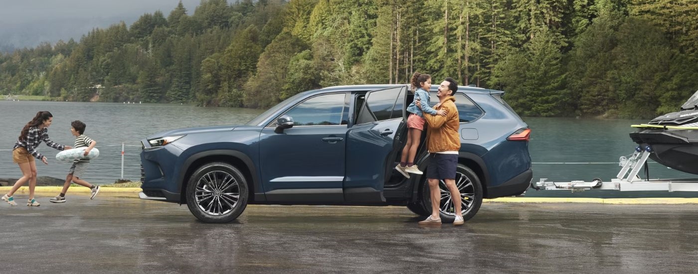 A blue 2024 Toyota Grand Highlander is shown from the side parked near a lake.