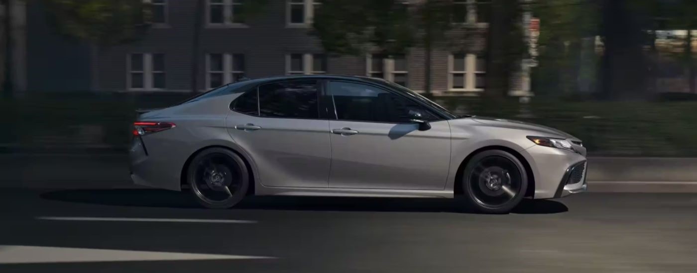 A silver 2022 Toyota Camry is shown form the side driving on a city street.