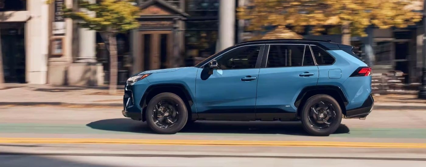 A blue 2023 Toyota RAV4 XSE is shown from the side driving on a city street.