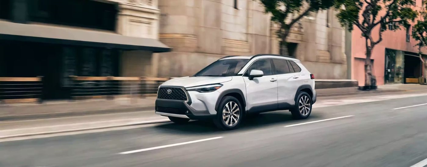 A white 2023 Toyota Corolla XLE is shown driving on a city street after leaving a New Rochelle Toyota dealer.