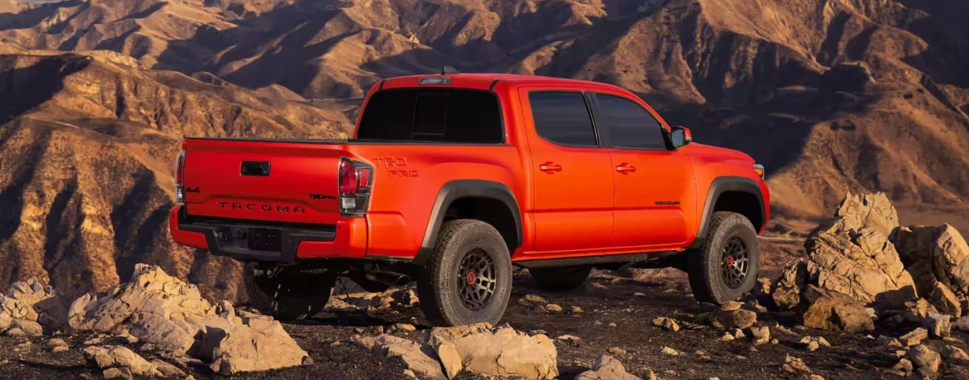 An orange 2023 Toyota Tacoma TRD Pro is shown from the rear parked in a rocky mountain area.