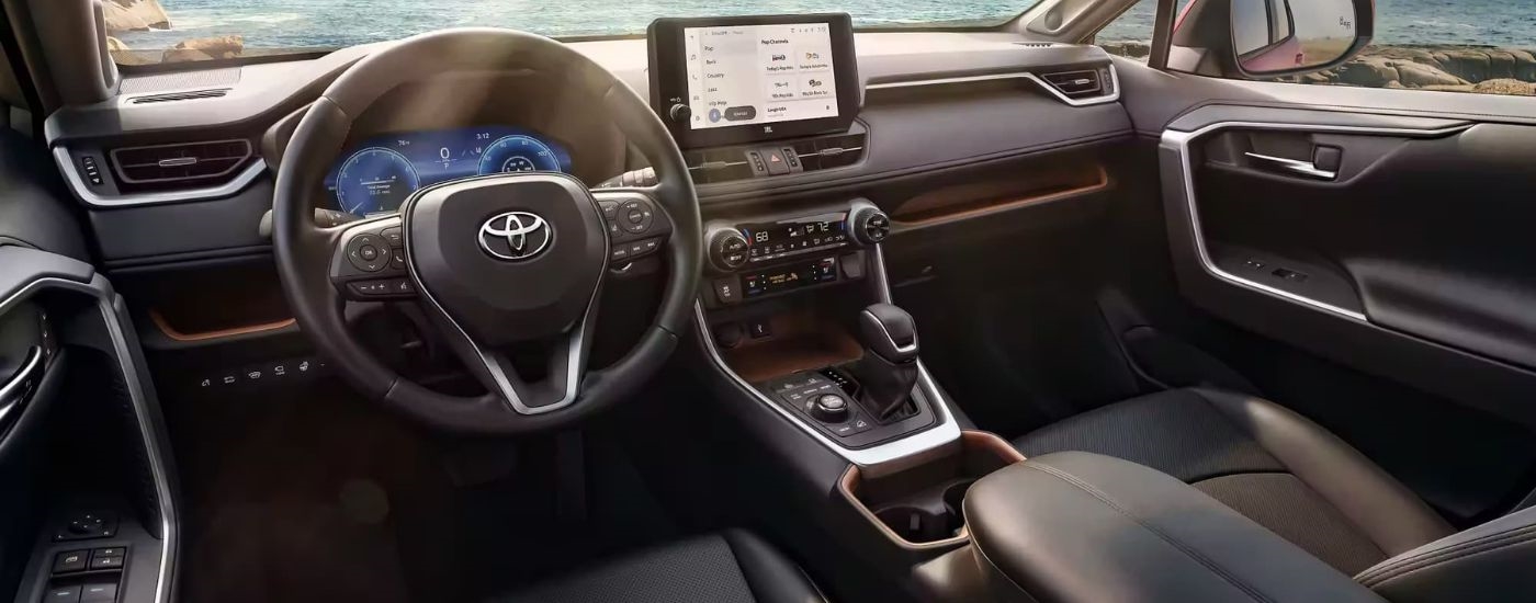 The black interior of a 2024 Toyota RAV4 is shown from the driver's seat.