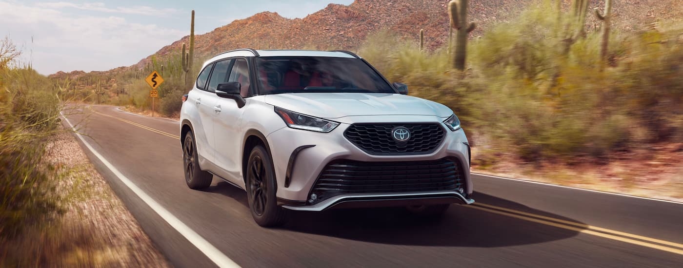 A white 2024 Toyota Highlander XSE is shown driving in a desert after visiting a dealer with a Toyota Highlander for sale.