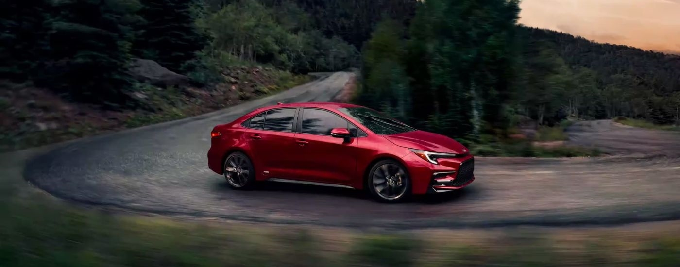 A red 2024 Toyota Corolla Hybrid SE driving on a winding mountain road.