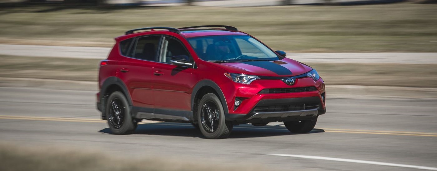 A red 2018 used Toyota RAV4 for sale is shown driving on an open road.